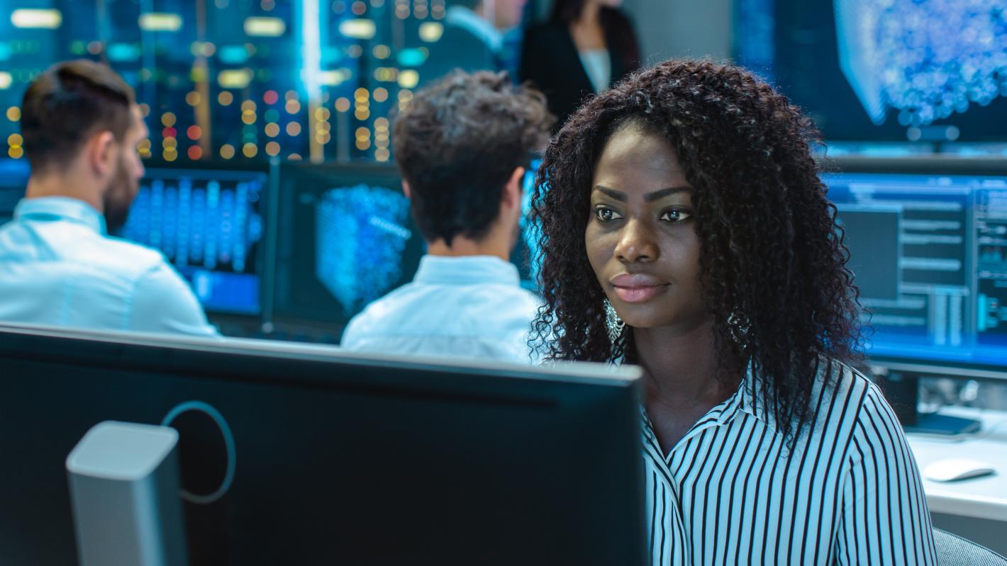 individuals sitting in front of computer monitors displaying various graphs and data, suggesting surveillance of safety and security