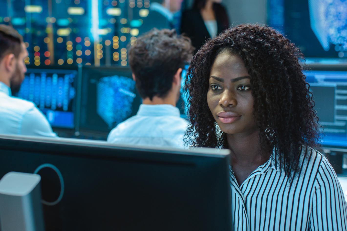 individuals sitting in front of computer monitors displaying various graphs and data, suggesting surveillance of safety and security
